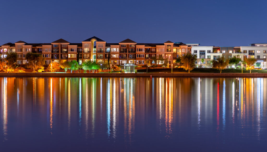 The multi-hued lights of stylish condos reflect off the calm waters of Tempe Town Lake in Tempe, Arizona.