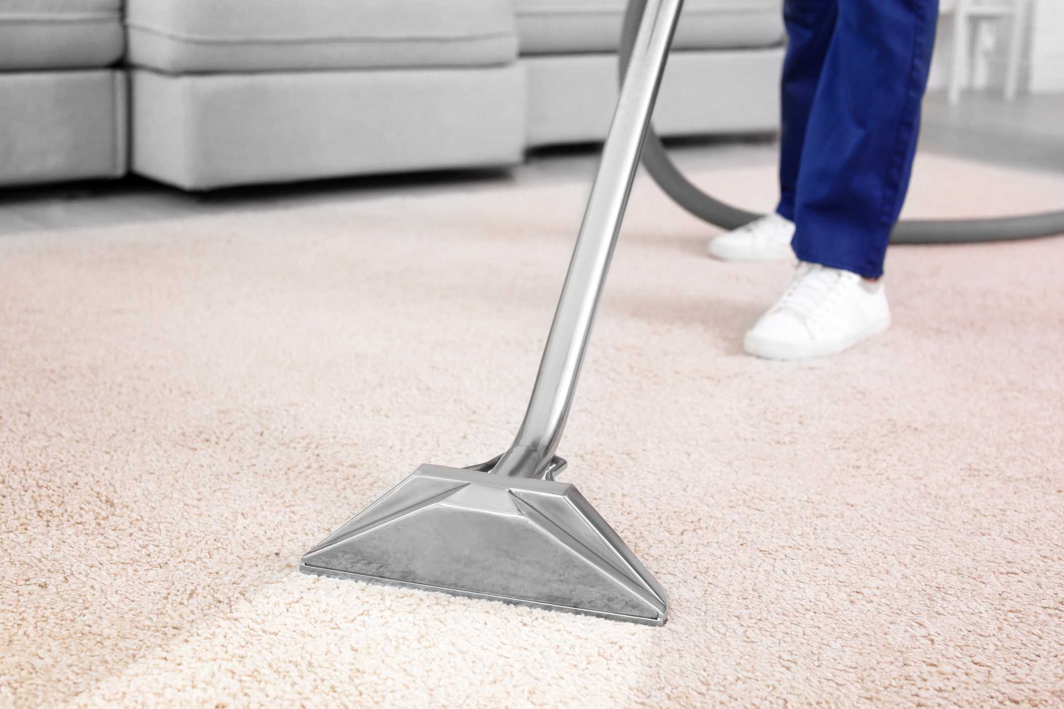 An individual uses a vacuum to clean their white carpet